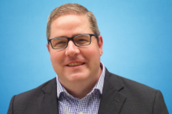 White male with short hair and gray blazer with checked button down shirt