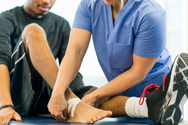 2 males, one applying tape to ankle of the other 