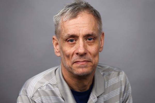 Headshot of a person wearing striped gray and white polo with short, gray hair.