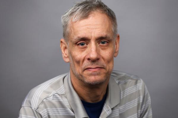 Headshot of a person wearing striped gray and white polo with short, gray hair.