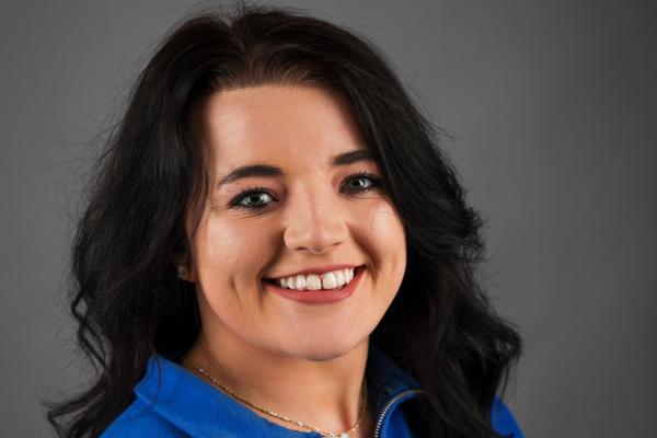 Headshot of a person waring a blue t-zip with long dark hair.