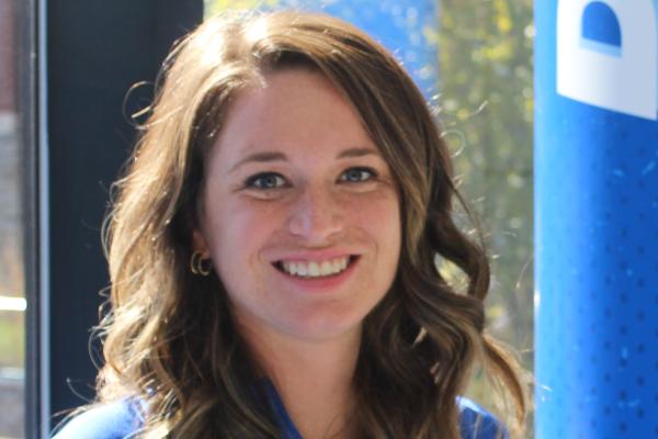 A woman with brown hair and a blue shirt sits smiling