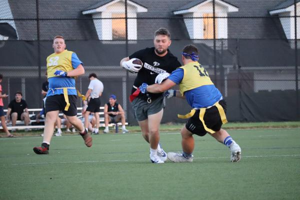 Intramural Sports flag football game in progress three players with one player running with the football and another reaching for the players flag
