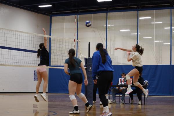 Four students playing indoor volleyball with intramural sports. One is spiking the ball while the opponent is trying to block
