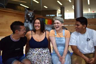 Four students sitting on the Gatton Student Center Social Staircase with Wildcat statue in the background