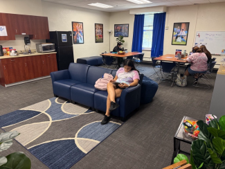 Students sit a tables and on a couch studying with a kichnette in the background.