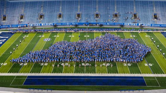 Thousands of students wearing blue arranged in the outline of the state of Kentucky on Kroger Field