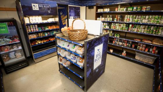 Interior view of the Big Blue Pantry with cans and boxes of food lining the shelves. In the middle of the pantry is a dark colored shelf that has food around the outside.