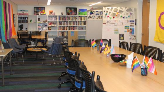 The interior of the Dinkle-Mas Suite with tables, chairs, pride flags, a gazebo, and a lending library.