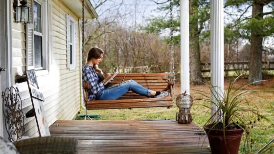 Female sits on a porch swing while working on her laptop.