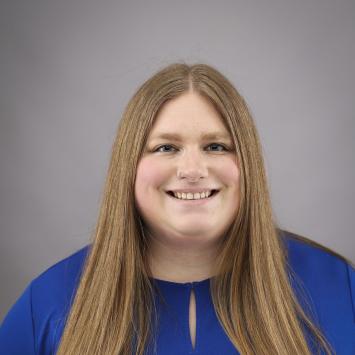 An image of a woman smiling with long blonde hair and wearing a blue shirt.