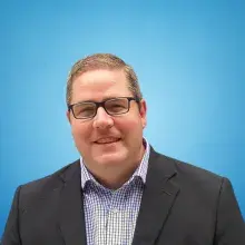 White male with short hair and gray blazer with checked button down shirt