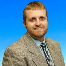 Male with blonde short hair in a blazer, tie and blue buttondown shirt