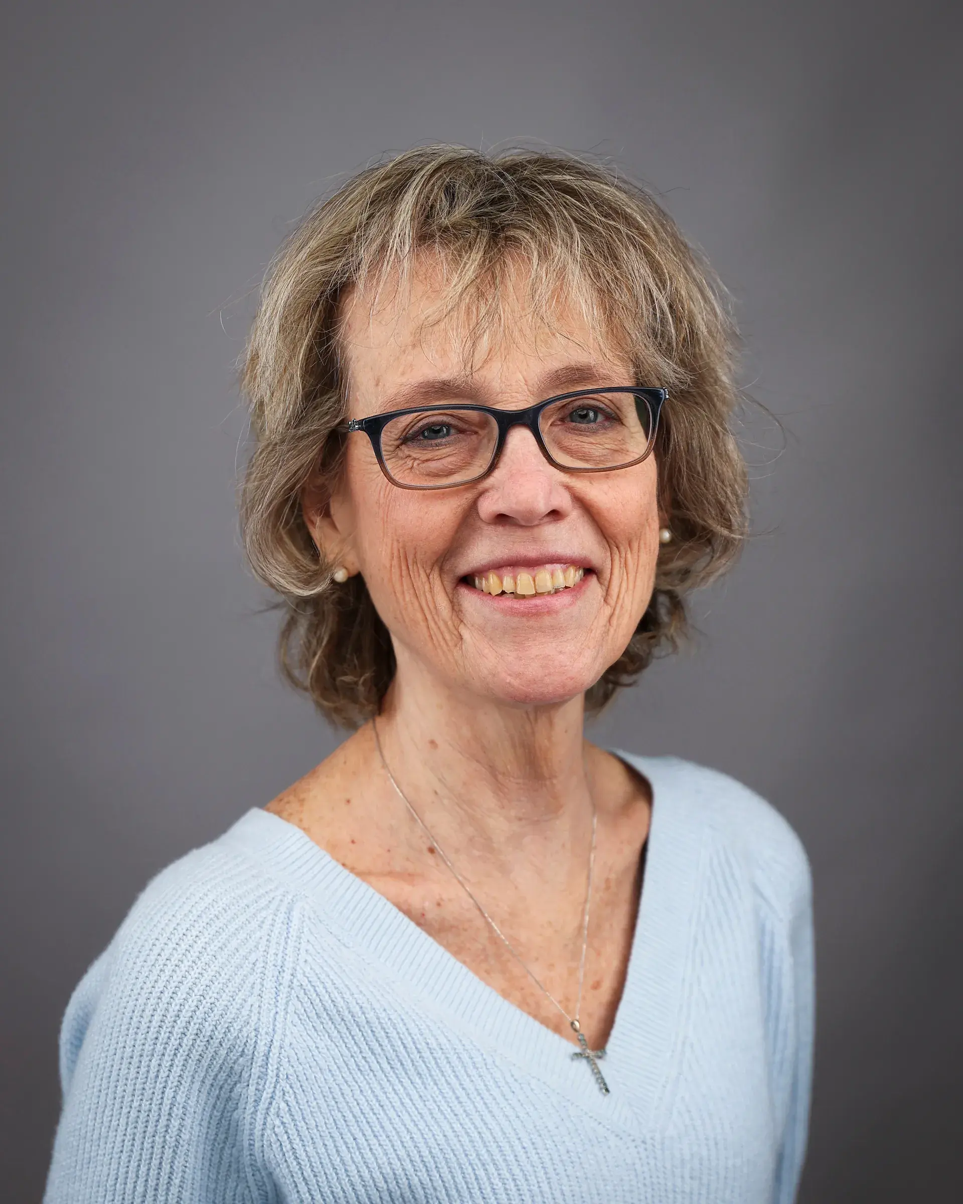 Headshot of a person with short blonde hair, wearing dark rimmed glasses.