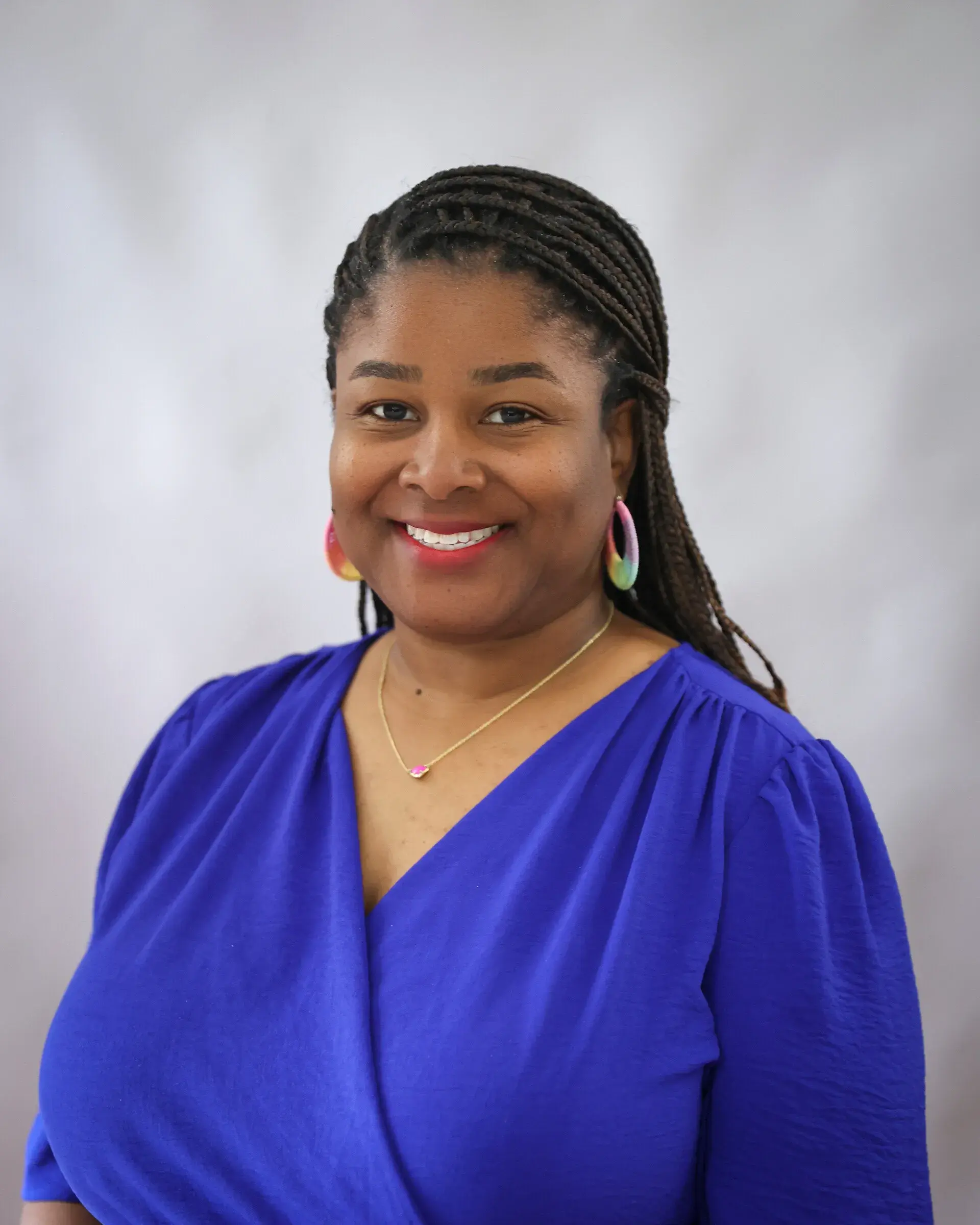 Person wearing a blue dress with braided hair and colorful earrings.