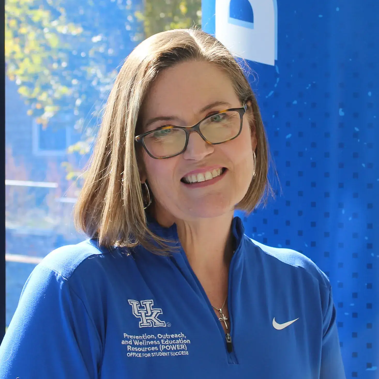A woman with blonde hair and a blue shirt sits smiling