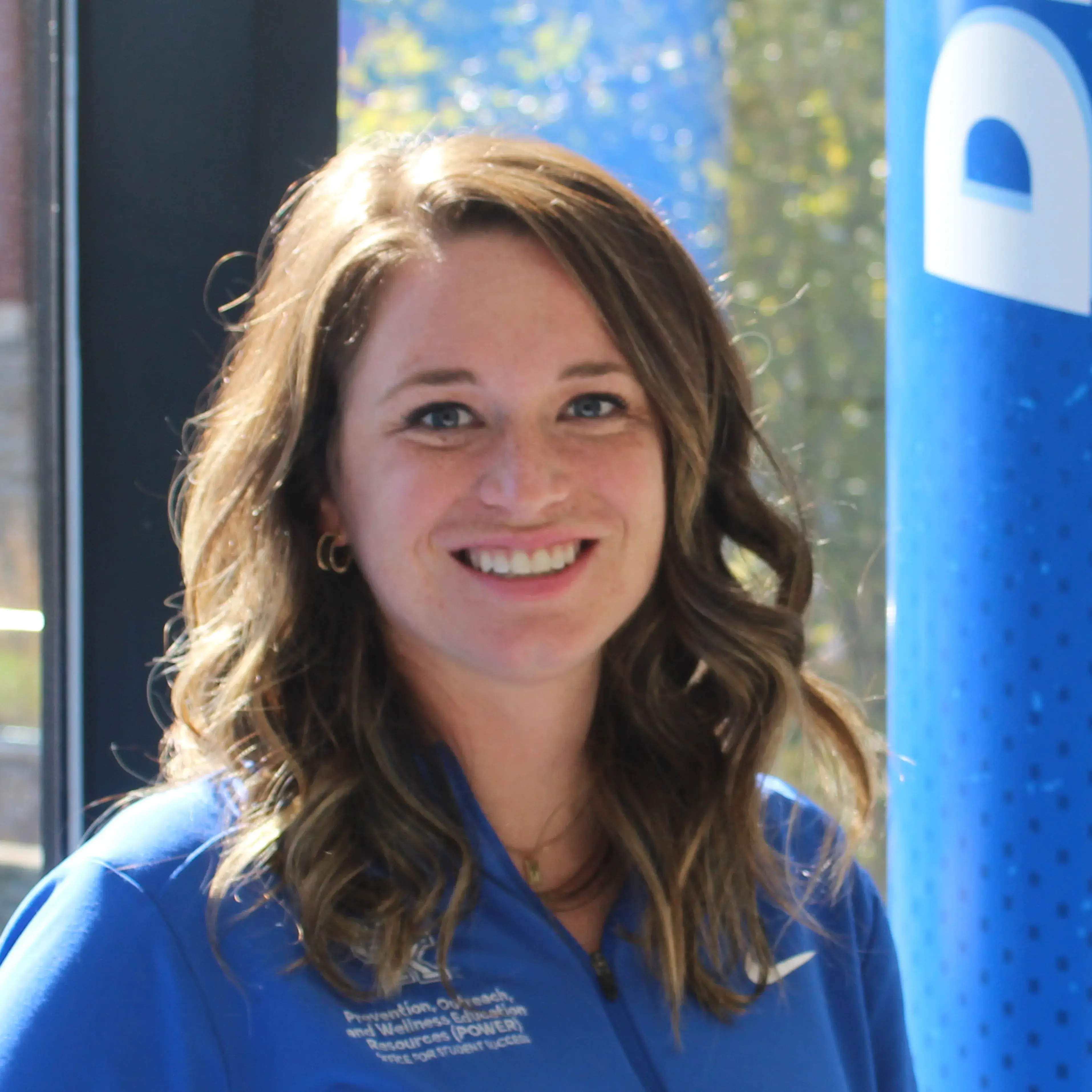 A woman with brown hair and a blue shirt sits smiling