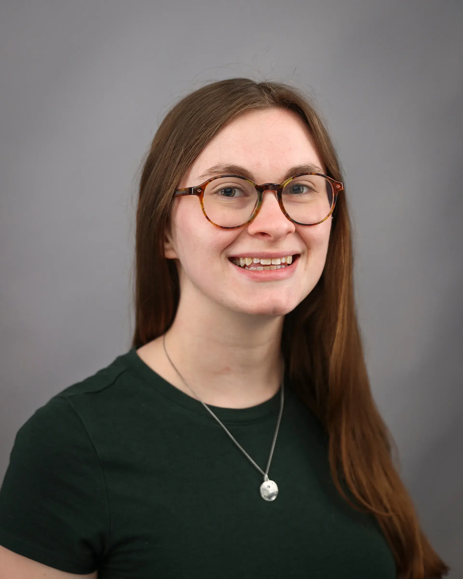 Headshot of a female with long brown hair wearing dark rimmed glasses and wearing a dark green top.