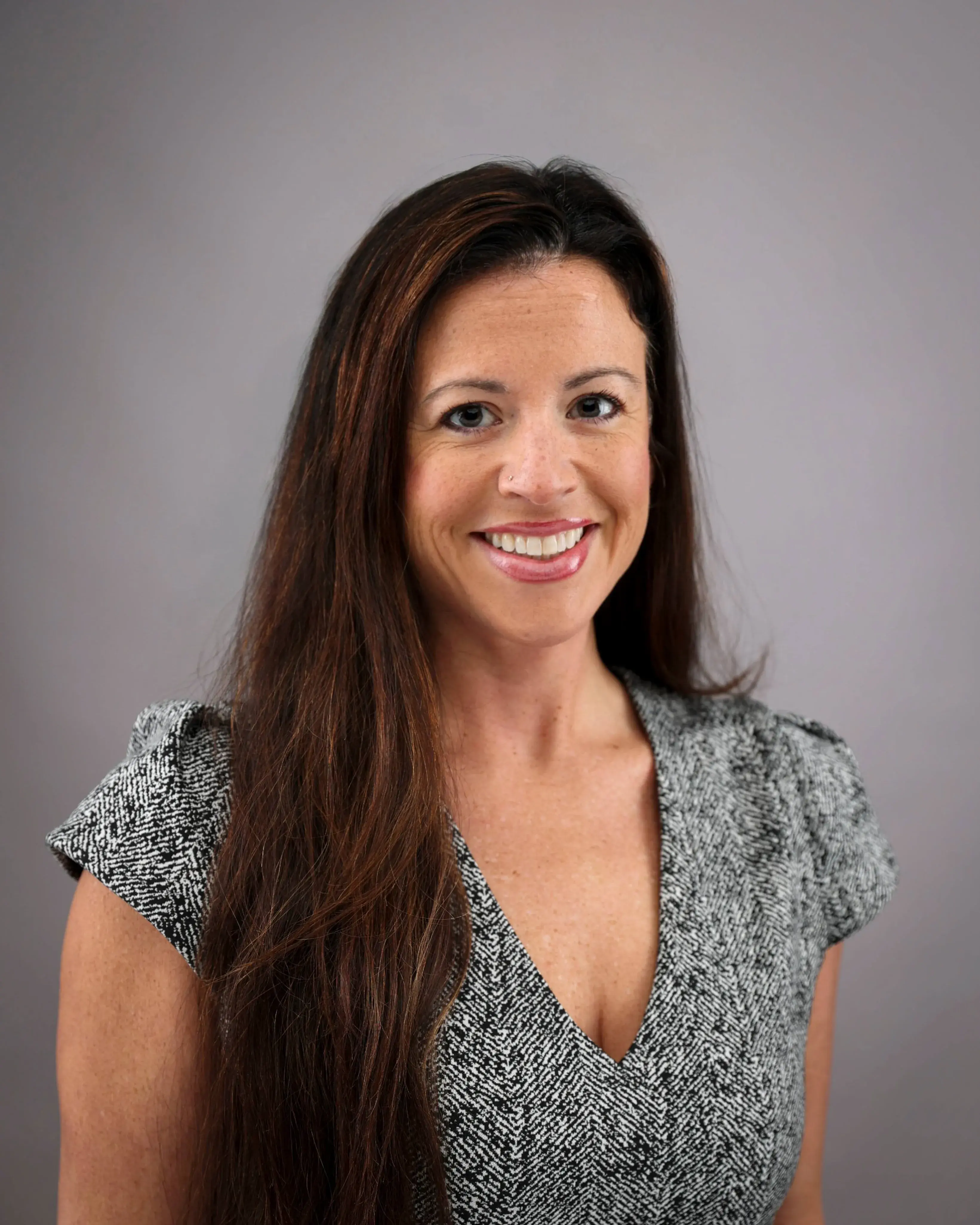 Headshot of a female with long brown hair wearing a short sleeved black and white blouse.